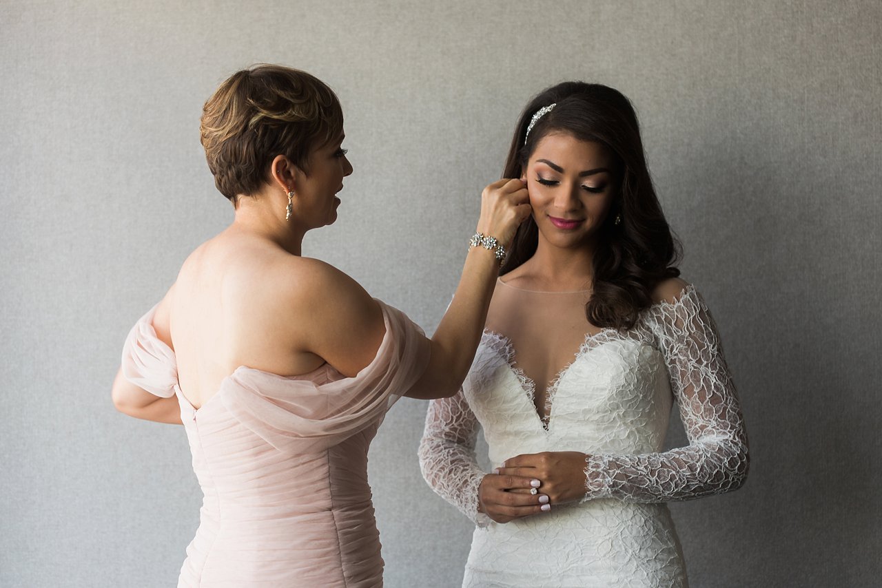 Bridesmaid in off-shoulder blush dress assisting bride with prep for wedding day