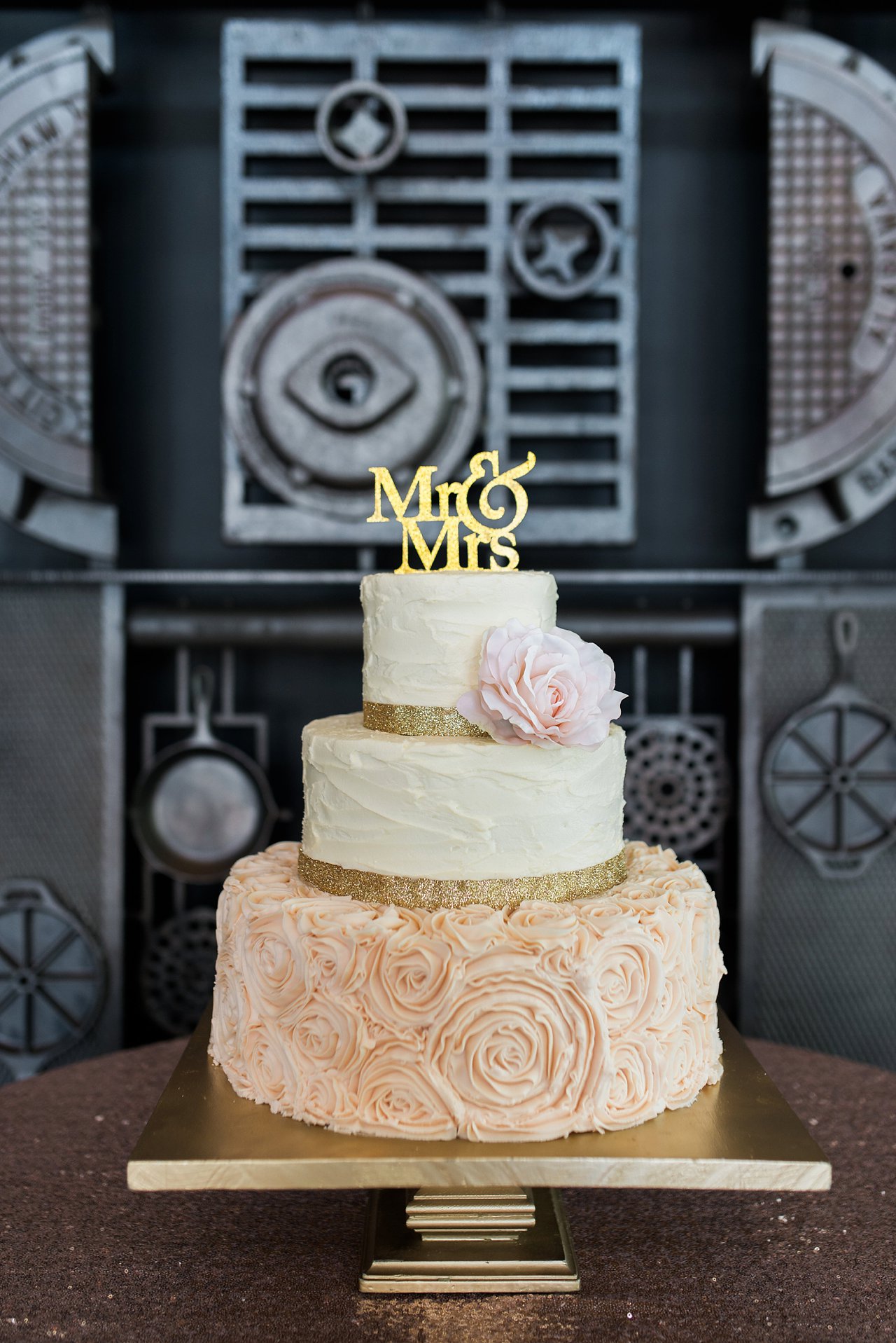 Rose gold and blush wedding cake against industrial back ground, featuring fresh flowers and iced rosettes by Olexa's Cakes in Birmingham, Alabama.